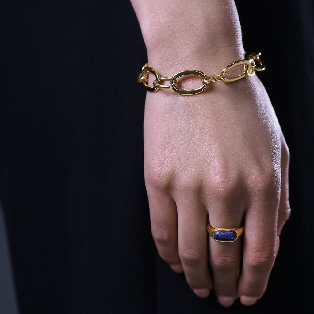 Gold bracelet and ring on a hand against a black background
